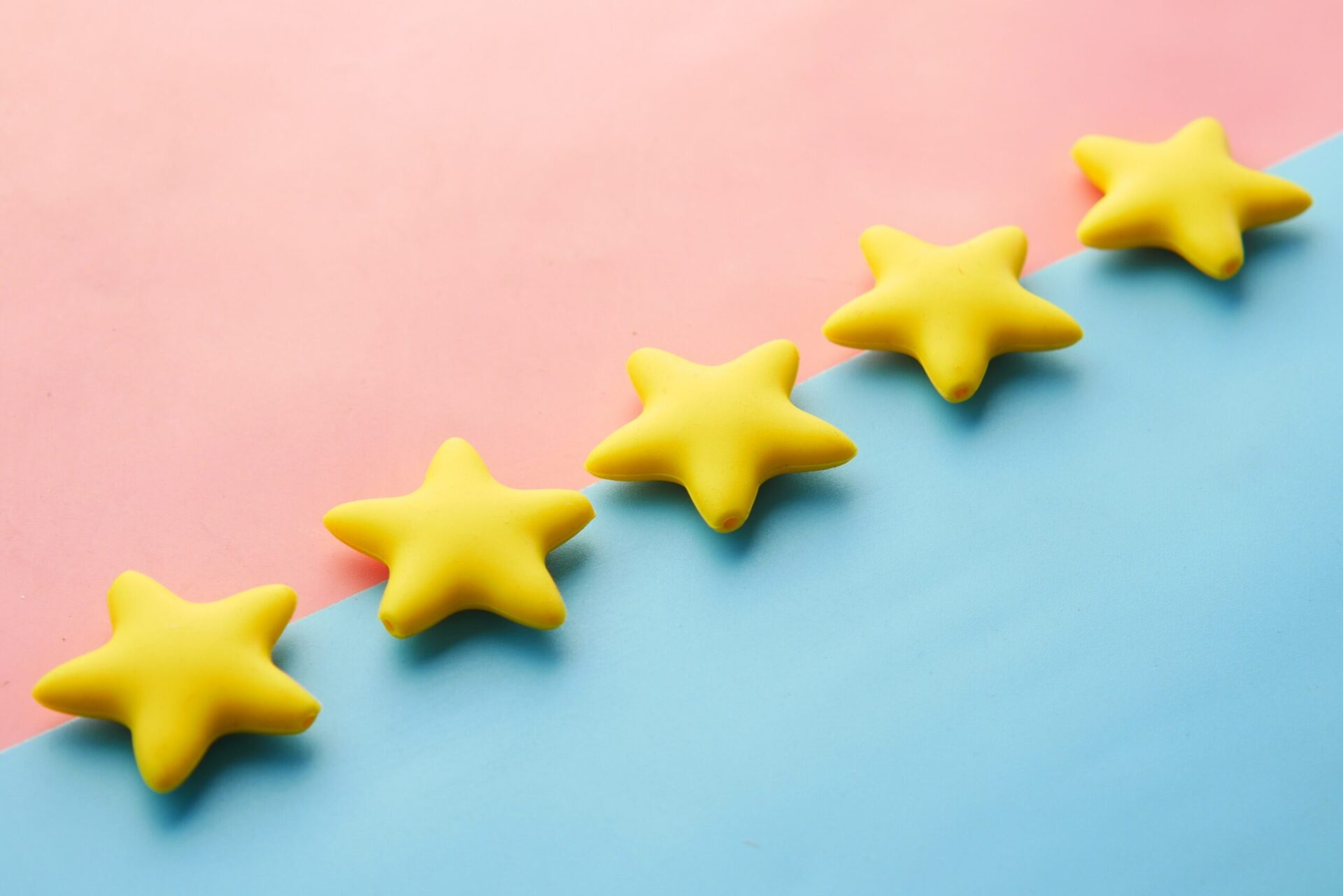 Five yellow stars lined up diagonally on a pink and blue background, representing a five-star customer rating and customer loyalty