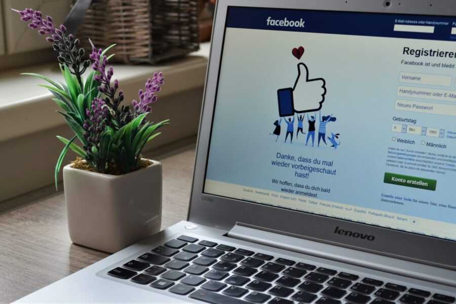 Laptop displaying the Facebook sign-up page next to a small potted lavender plant on a wooden desk