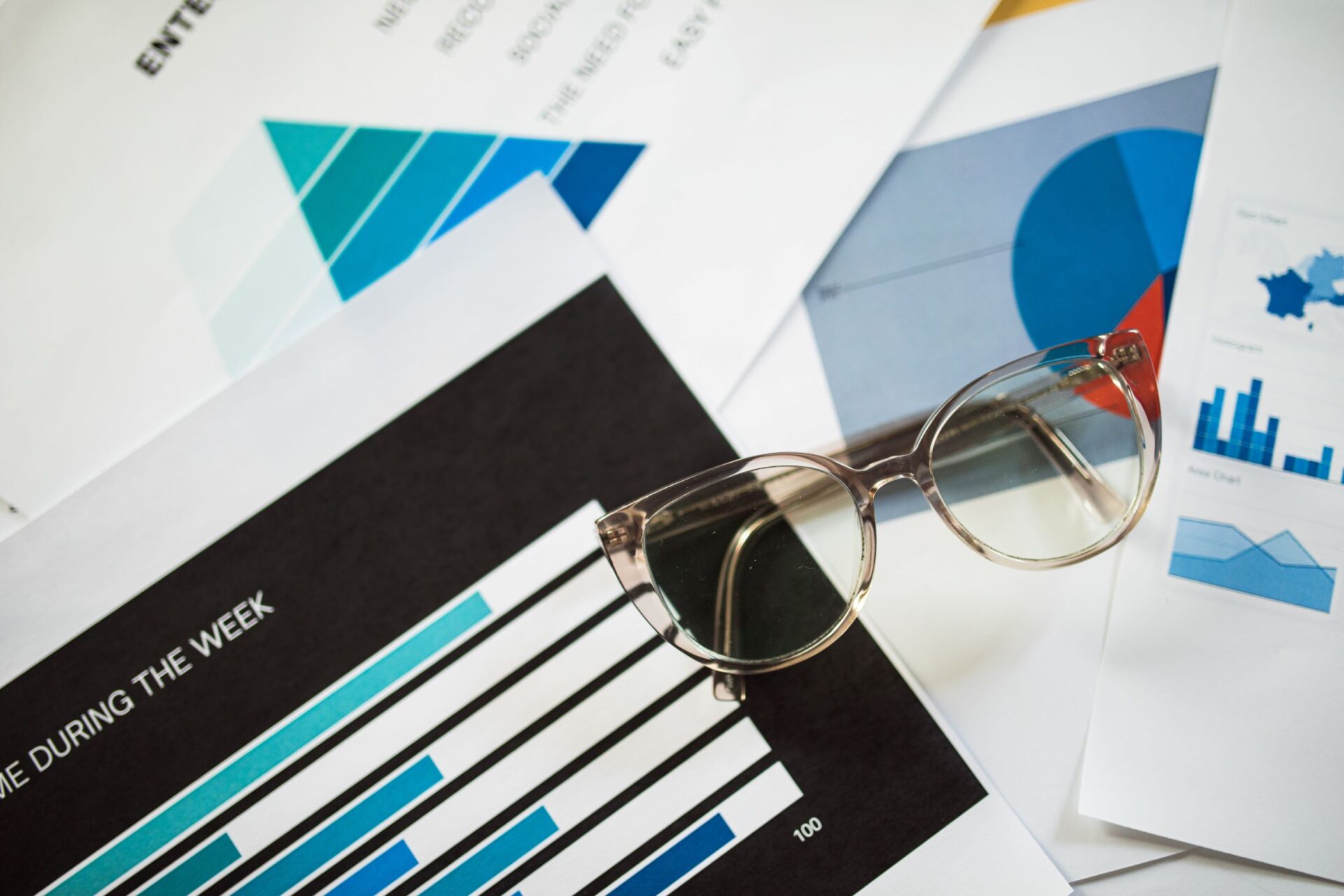 Printed infographics with bar and pie charts beside glasses, showing data visualization used in marketing