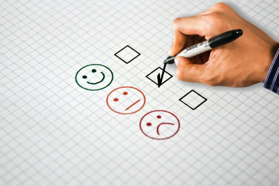 Hand checking a box beside a neutral face on a customer review rating scale with happy, neutral, and sad faces
