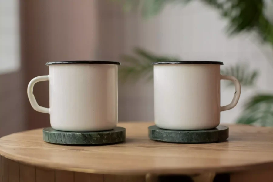 Two blank white enamel mugs on green marble coasters, ready for print on demand designs