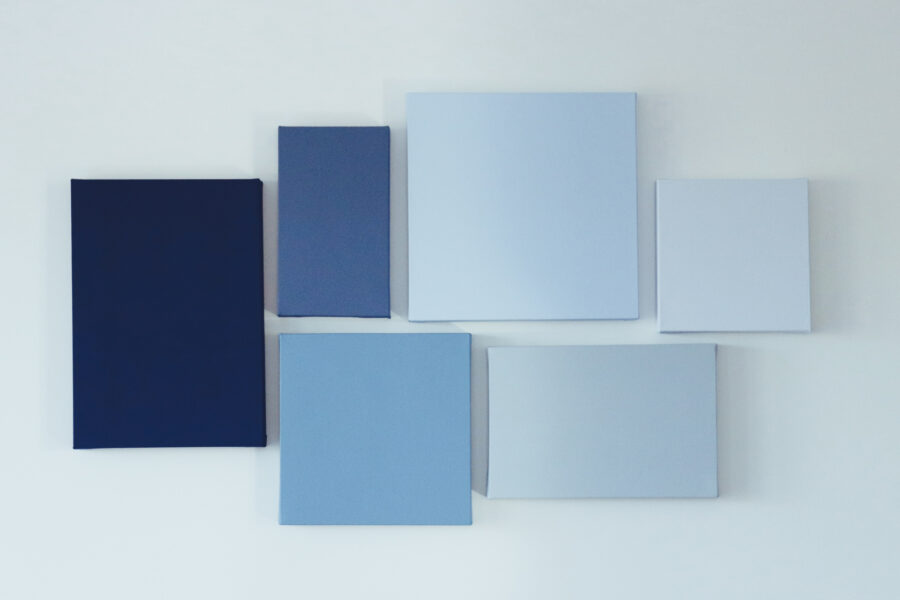 Stretched canvases in several sizes and blue tones arranged on a white wall