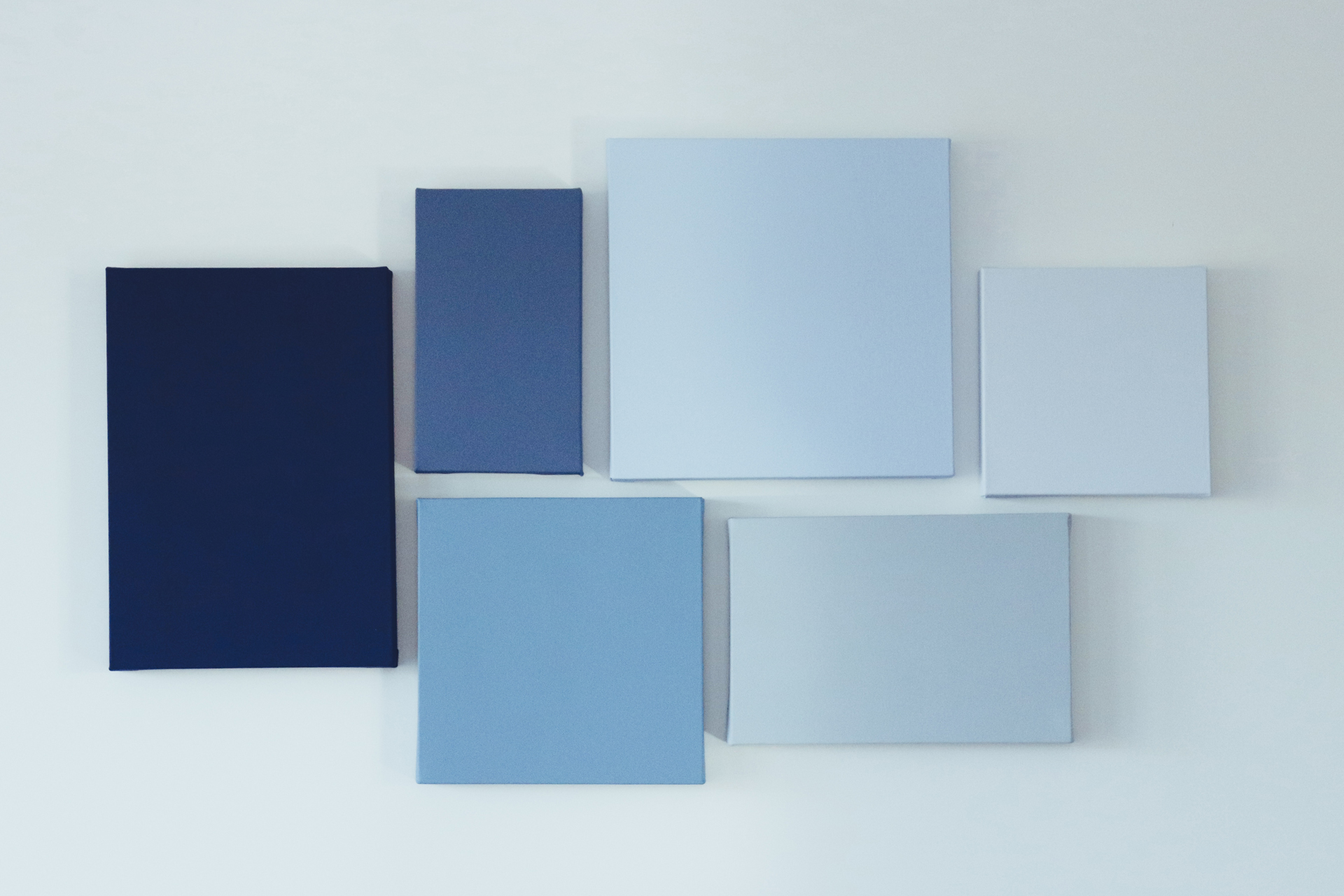 Stretched canvases in several sizes and blue tones arranged on a white wall