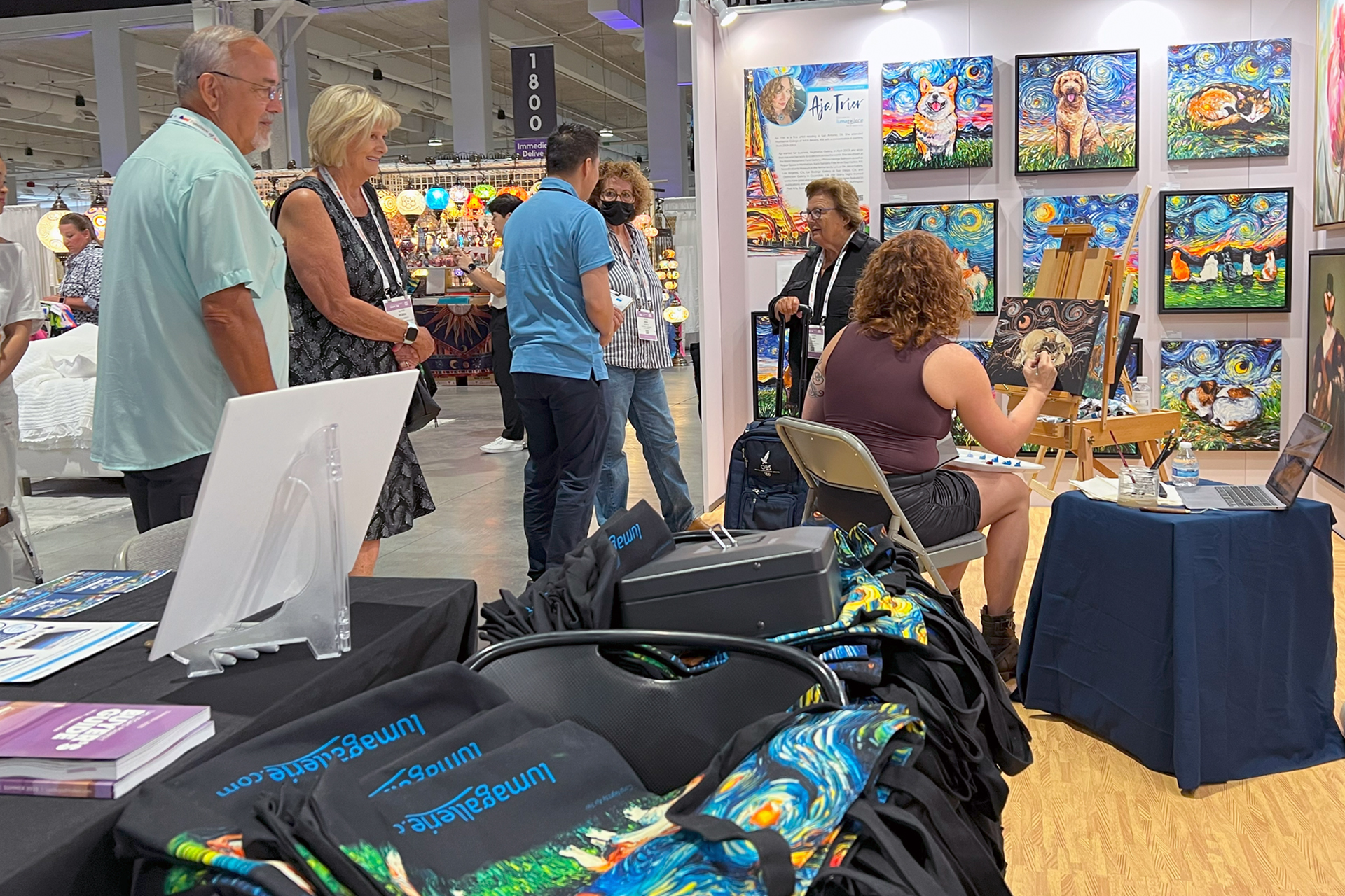 Lumaprints trade show booth at Las Vegas Market with canvas prints on display and an artist painting live