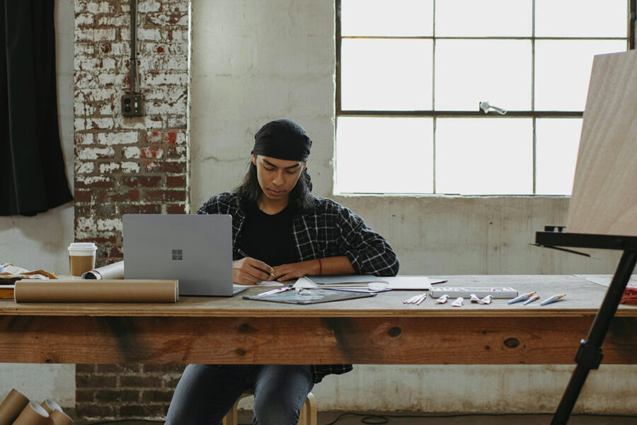 Artist planning new product options at a studio worktable with a laptop and print tubes nearby