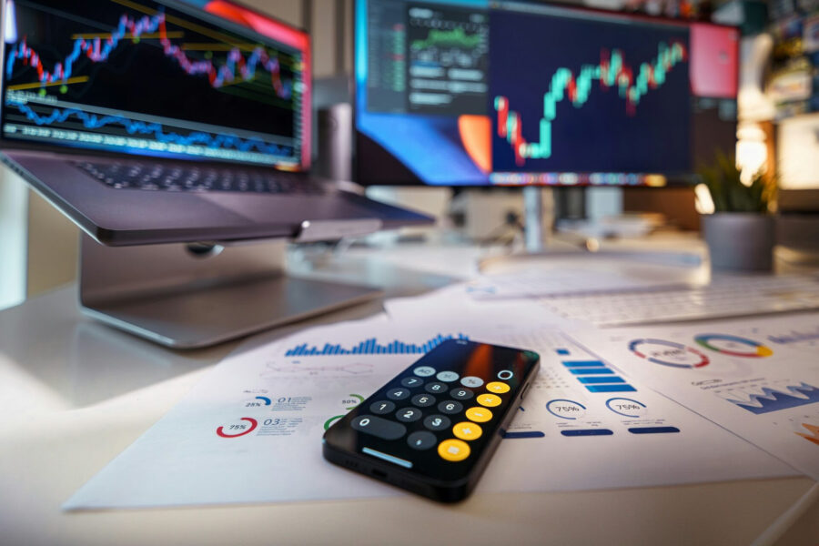 Calculator on sales reports beside screens showing charts, used to review pricing and profit margins