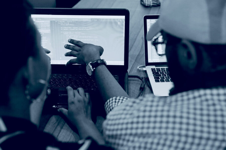 Two people reviewing code and automation setup on laptops while building a marketing workflow