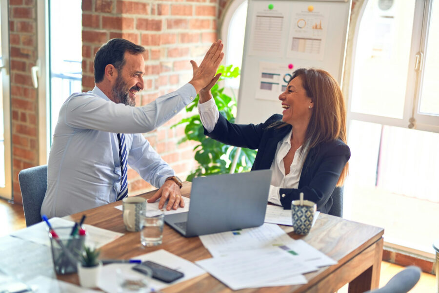 Business professionals high-fiving during a successful meeting with a laptop and reports