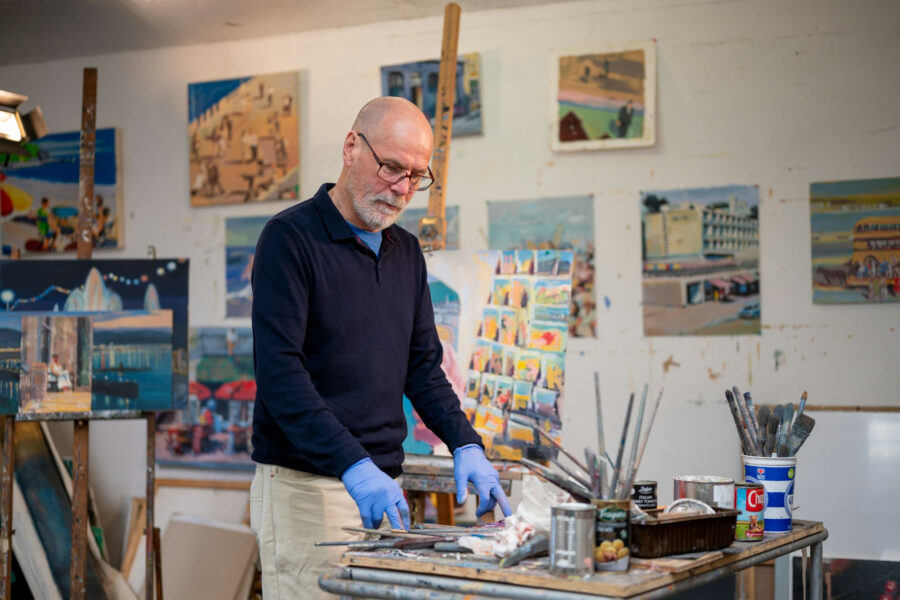 Artist working in a painting studio surrounded by colorful canvas artwork, brushes, and art supplies
