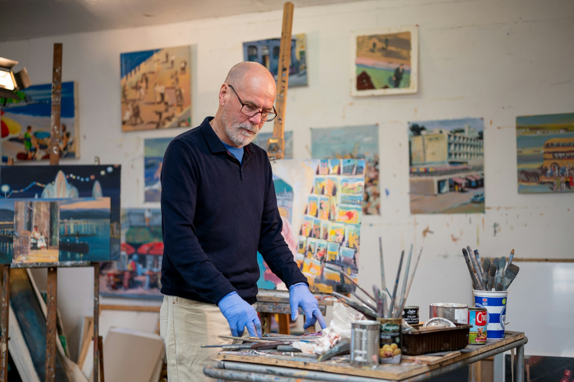 Artist working in a painting studio surrounded by colorful canvas artwork, brushes, and art supplies