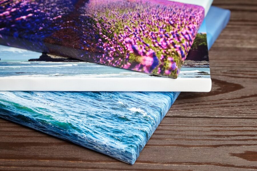 Stack of colorful canvas photo prints featuring lavender fields, coastal scenery, and ocean waves