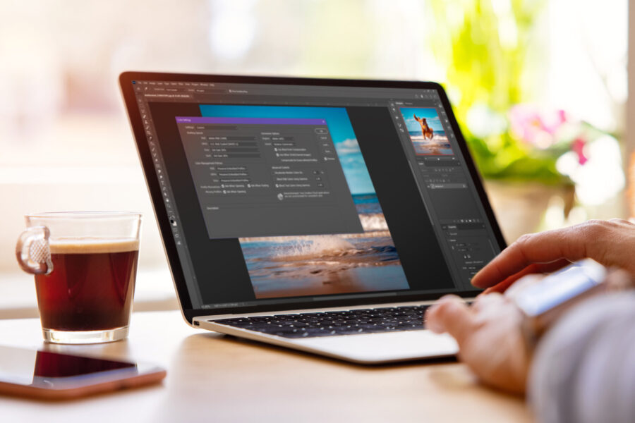 A person using photo editing software on a laptop next to a cup of coffee.