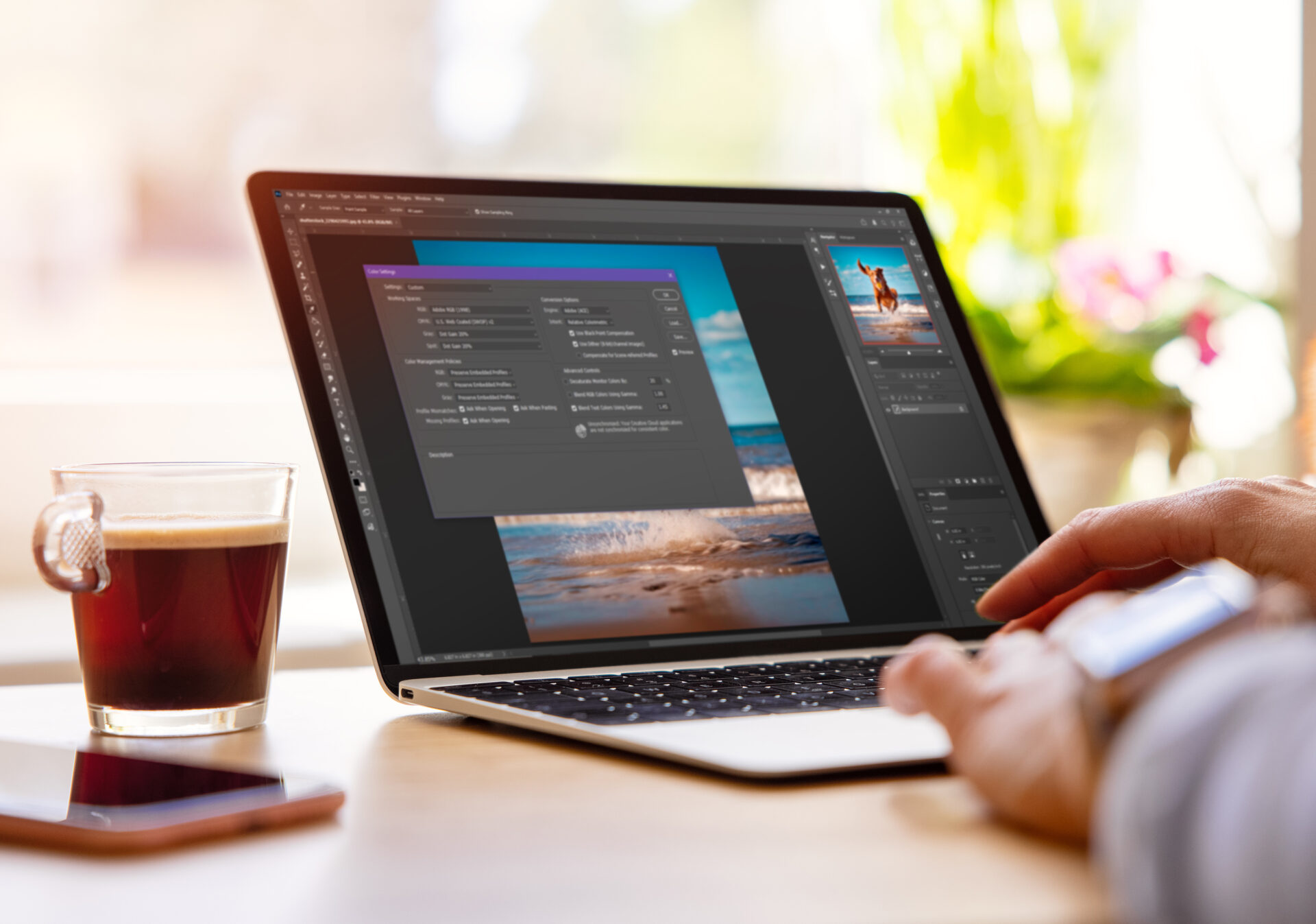 A person using photo editing software on a laptop next to a cup of coffee.