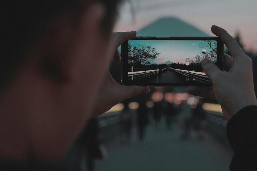 Person using a smartphone camera to photograph a mountain landscape at sunset.