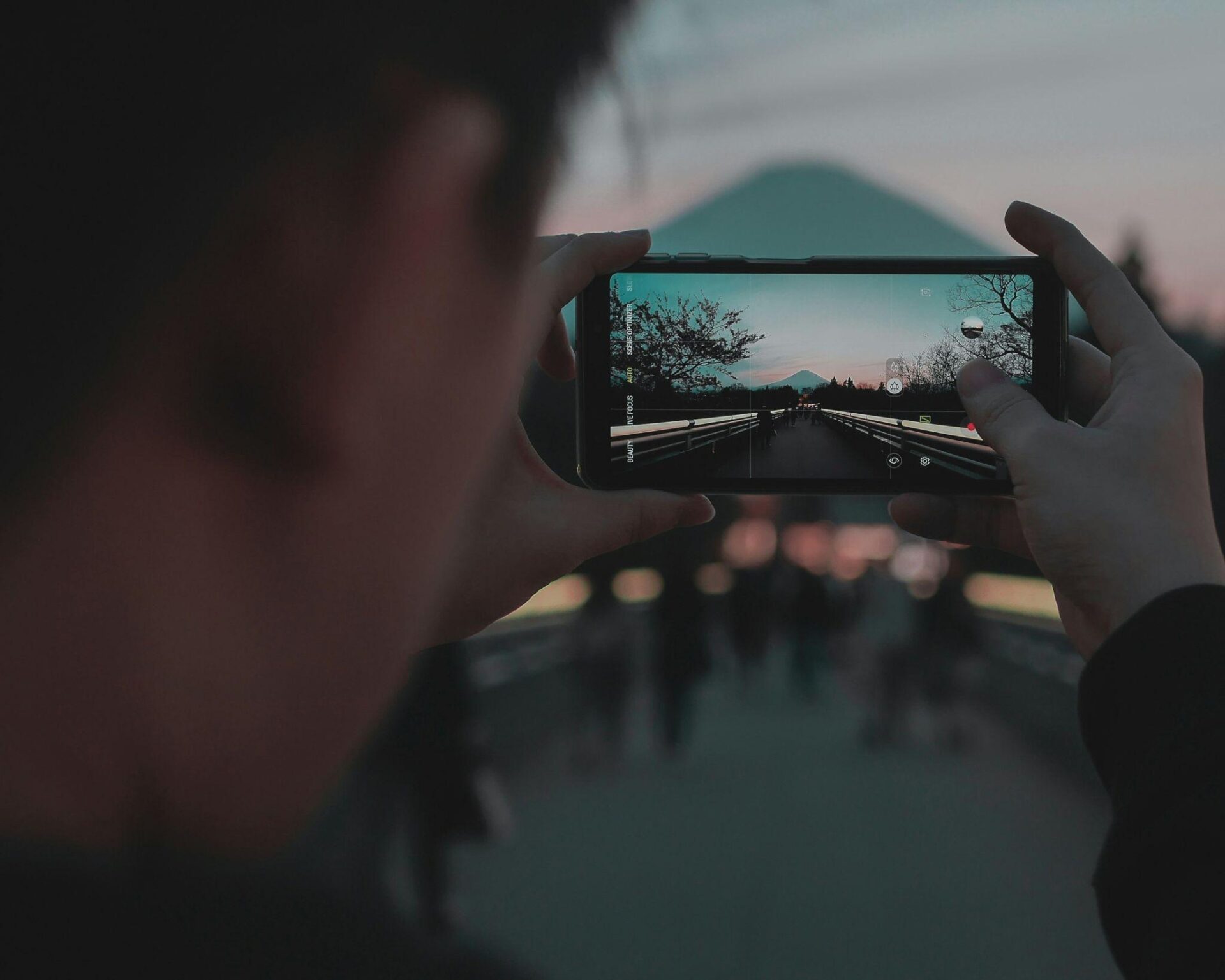 Person using a smartphone camera to photograph a mountain landscape at sunset.