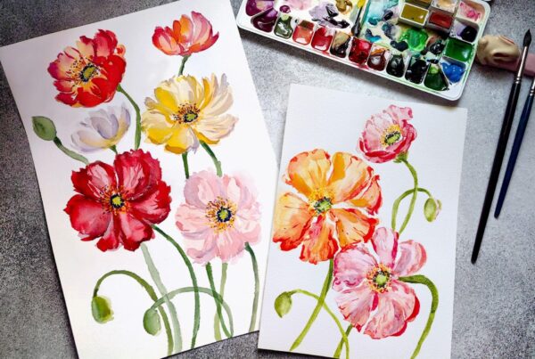 Two textured papers displaying watercolor floral paintings next to art supplies.